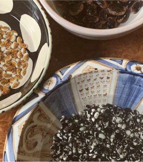 Three decorative bowls filled with various dried beans, including white and tan, dark brown, and black and white speckled.