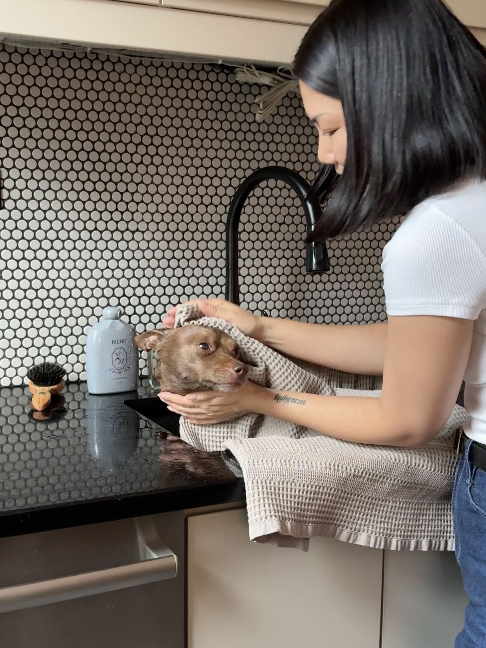 A woman drying a wet brown dog with a towel over a kitchen sink.
