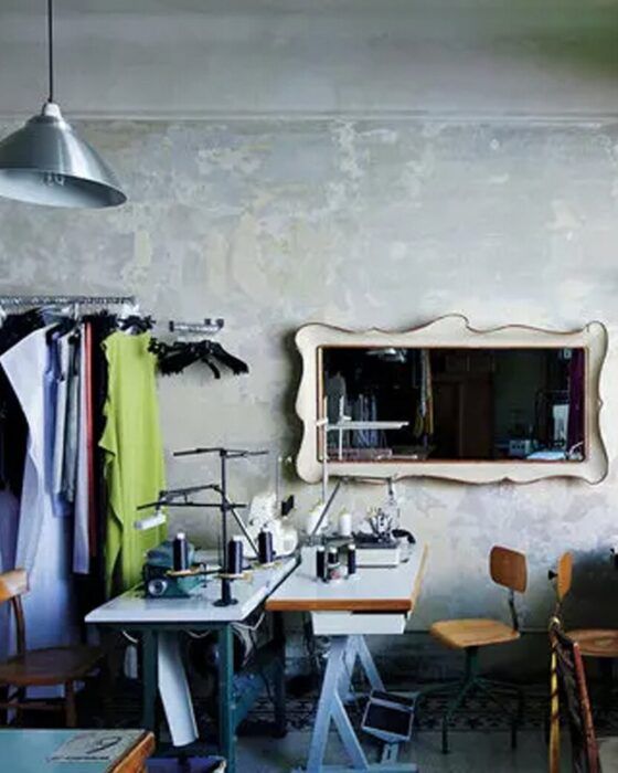 A sewing studio with two machines, a clothing rack, and a decorative mirror on a textured grey wall.