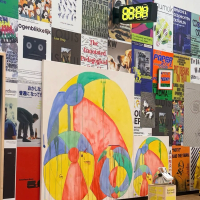 A wall filled with diverse posters displays a large painting of colorful, paint-dripped circles and a digital clock showing "88:88".