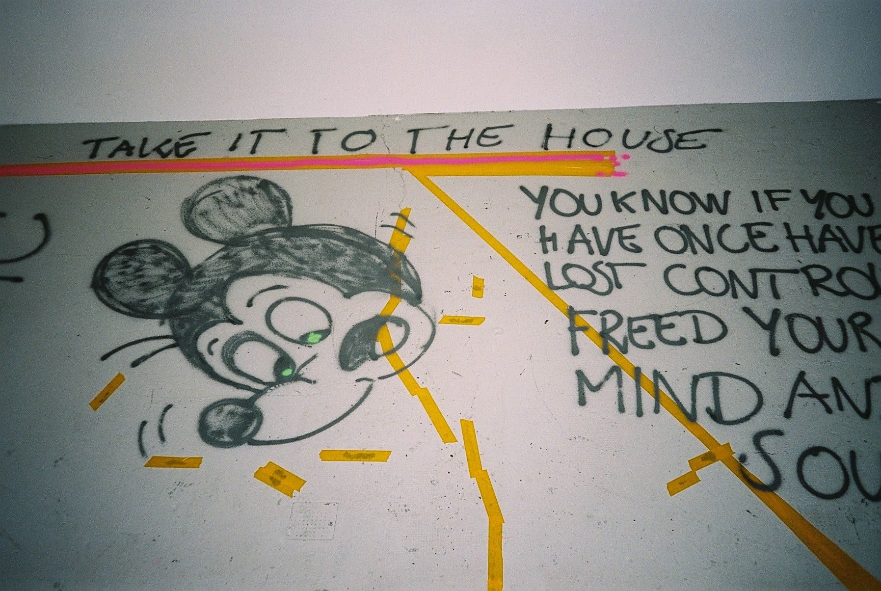 Graffiti of Mickey Mouse with green eyes, text "TAKE IT TO THE HOUSE" and partial text "YOU KNOW IF YOU HAVE ONCE HAVE LOST CONTROL FREED YOUR MIND AND SOU", highlighted with pink and yellow tape.