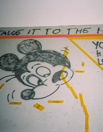 Graffiti of Mickey Mouse with green eyes, text "TAKE IT TO THE HOUSE" and partial text "YOU KNOW IF YOU HAVE ONCE HAVE LOST CONTROL FREED YOUR MIND AND SOU", highlighted with pink and yellow tape.