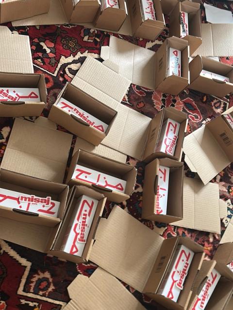 Many small cardboard boxes on a patterned rug, some open and containing white products branded "misaj" in red.