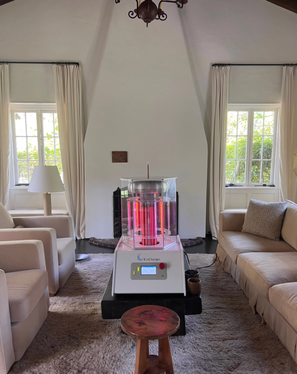 A white "BioChanger" device with a glowing red interior sits in front of a fireplace in a living room with couches and armchairs.