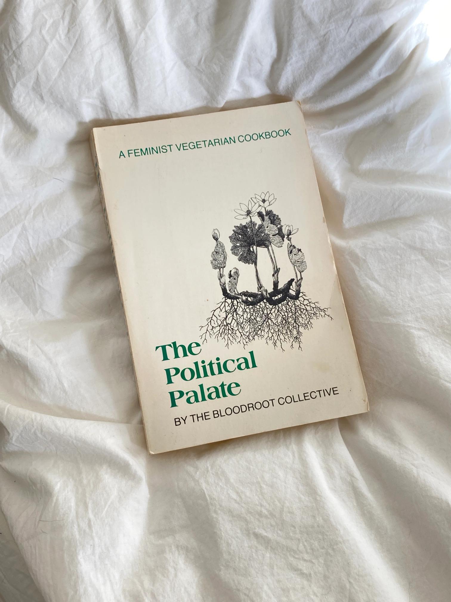 Book titled "The Political Palate: A Feminist Vegetarian Cookbook" by The Bloodroot Collective, on white wrinkled fabric.