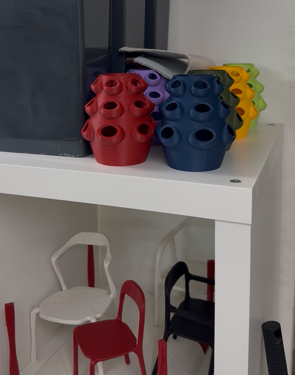 Colorful vertical planters and miniature chairs on a two-tier shelf.