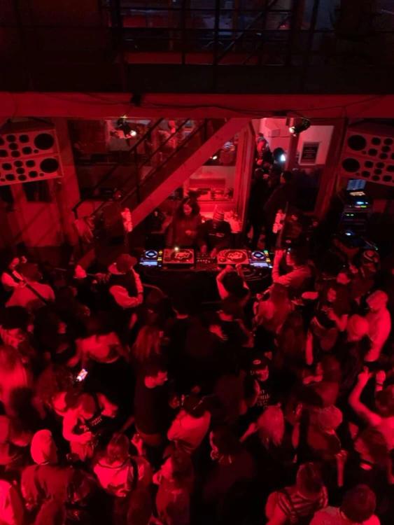 Overhead view of a crowded club, lit in red, with people dancing and a DJ working the booth.