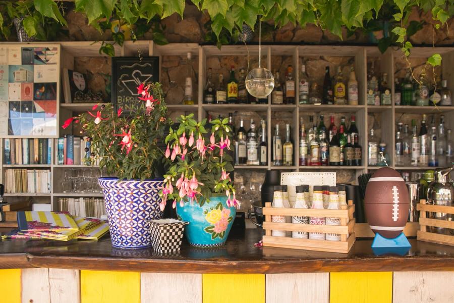 A colorful bar counter with blooming fuchsia plants, a football shaker, and shelves filled with liquor bottles.