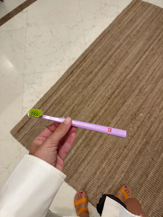 A person holds a purple Curaprox toothbrush with neon green bristles over a tiled floor and brown rug.