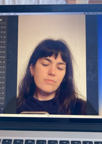 A woman with dark hair and bangs looking down, displayed on a laptop screen with the keyboard in the foreground.