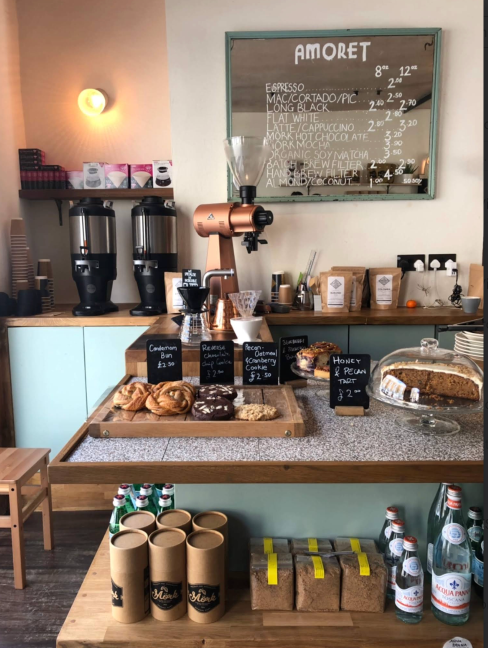 Two smiling baristas behind a coffee shop counter.