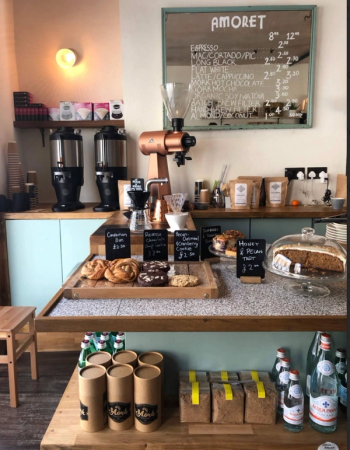 Two smiling baristas behind a coffee shop counter.