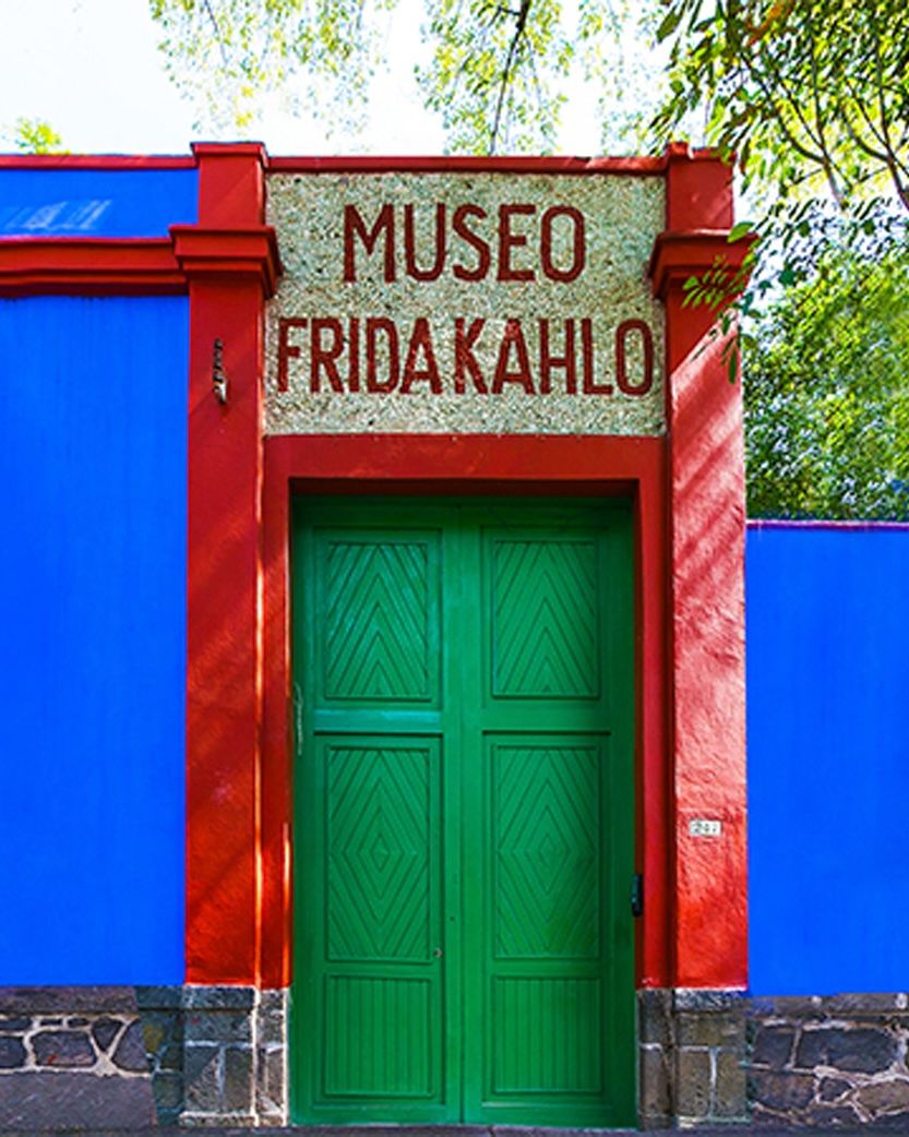 A vibrant blue building with red trim and green double doors, topped by a sign reading 'MUSEO FRIDA KAHLO'.