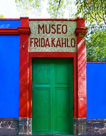 A vibrant blue building with red trim and green double doors, topped by a sign reading 'MUSEO FRIDA KAHLO'.