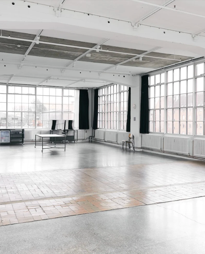 Spacious industrial studio with high ceilings, large grid windows, and mixed concrete and brick flooring.
