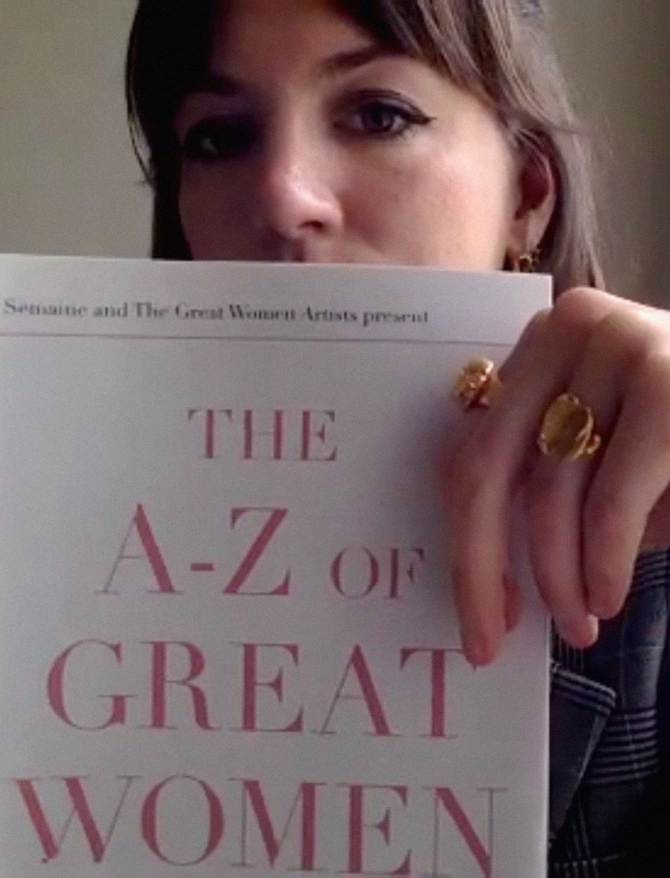 A woman holds a book titled "THE A-Z OF GREAT WOMEN" in front of her face.