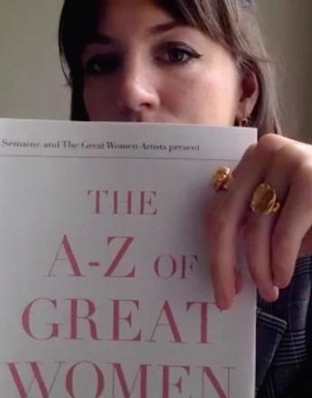 A woman holds a book titled "THE A-Z OF GREAT WOMEN" in front of her face.