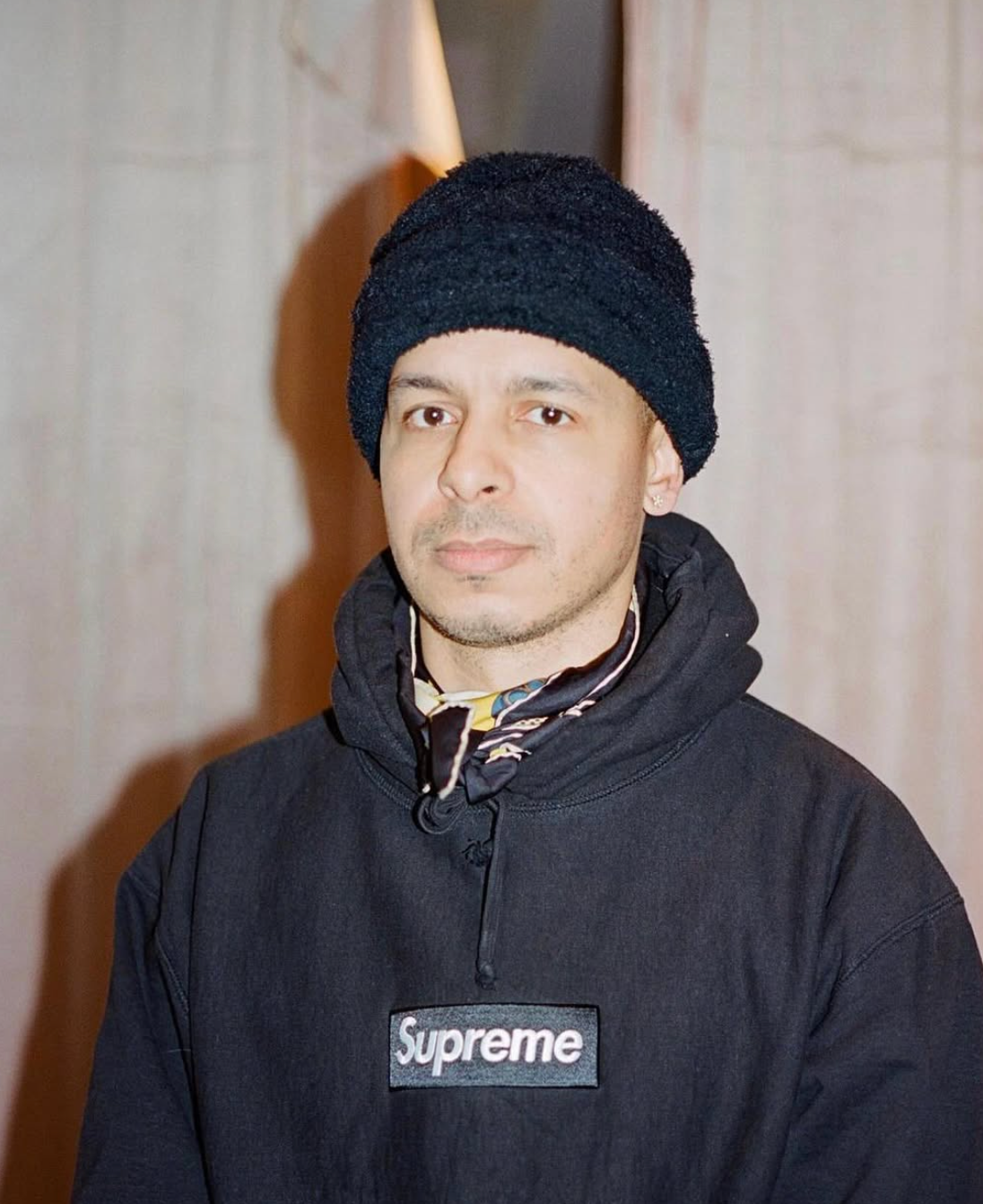 Silas Alder creative director of other circle copenhagen, black Supreme hoodie, and patterned scarf looks at the camera.