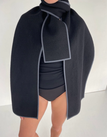 Person wearing a black felt cape and scarf with grey trim over black underwear and a top.