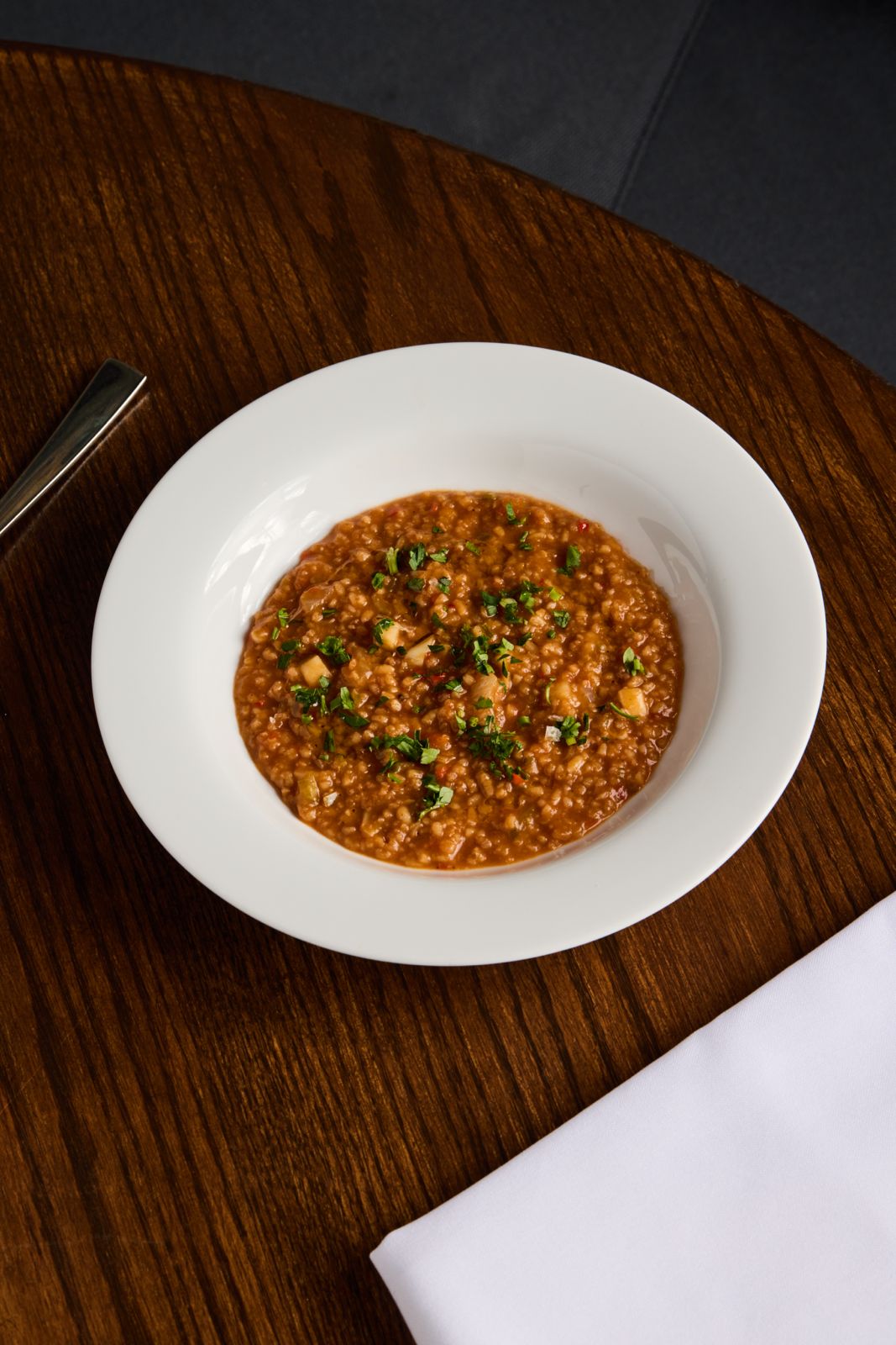 A white bowl of reddish-brown grain stew, garnished with herbs, on a wooden table.