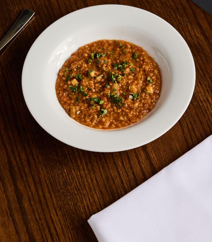 A white bowl of reddish-brown grain stew, garnished with herbs, on a wooden table.