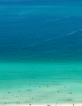 Aerial view of a beach with people swimming in clear turquoise water that transitions to a deep blue ocean.