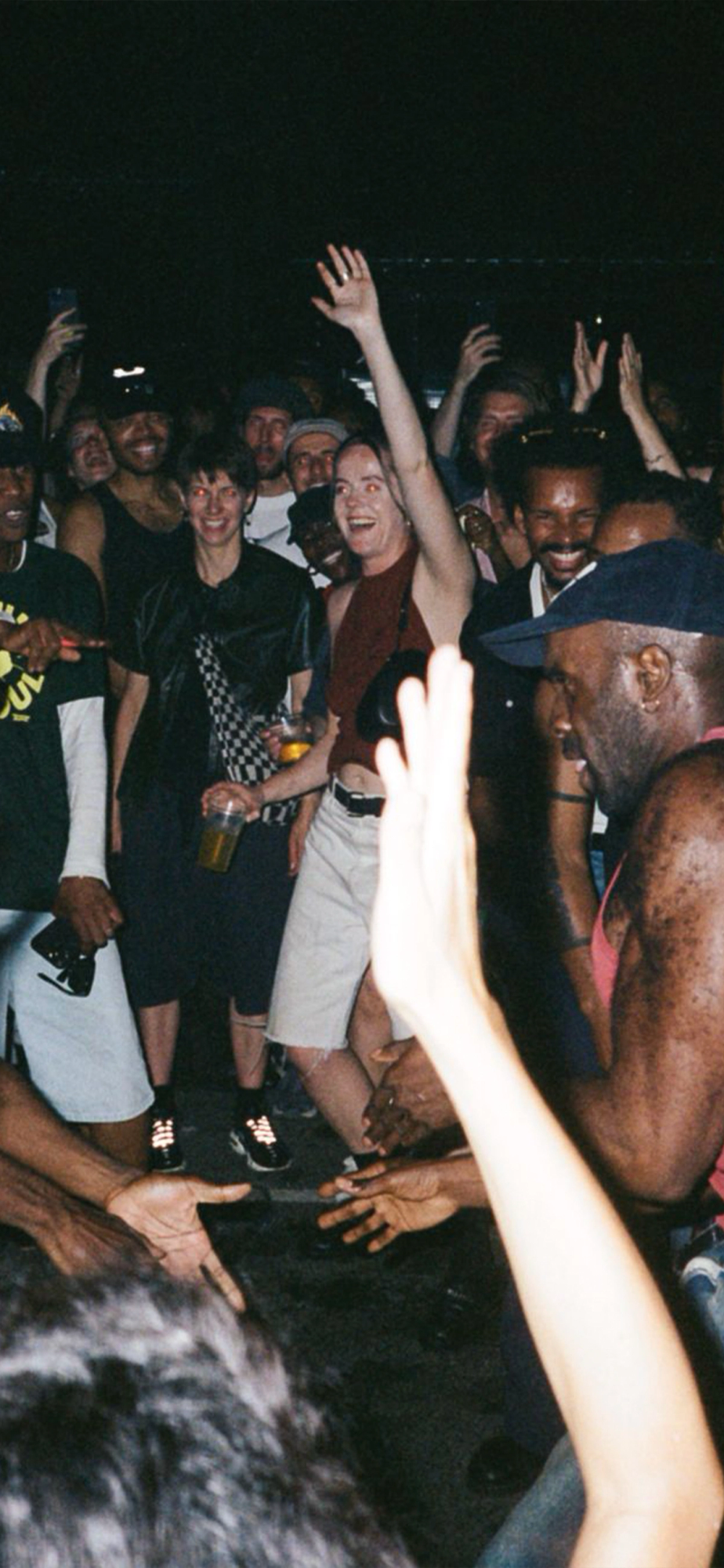 A large group of people dancing energetically in a dark room, with many arms raised.