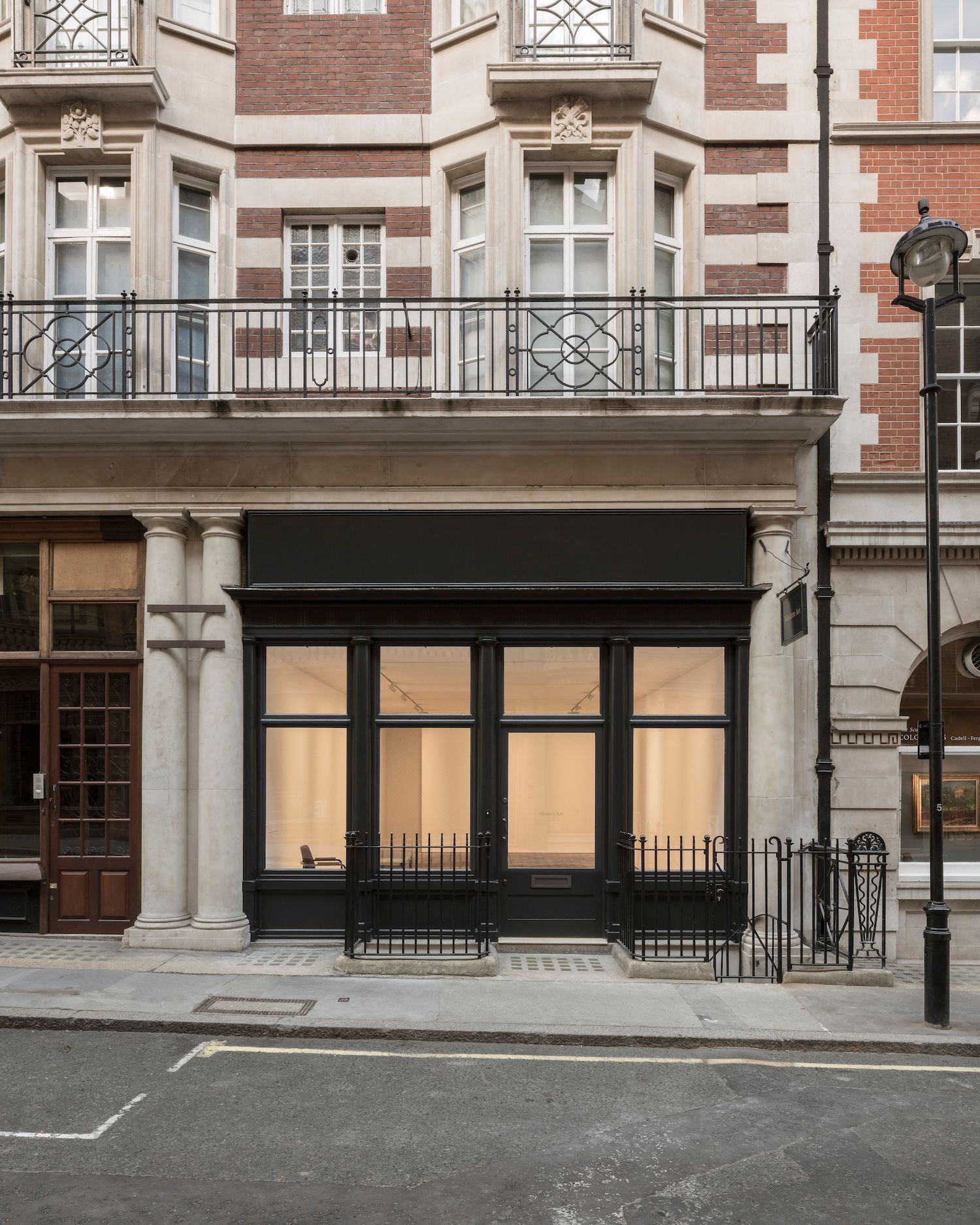 A black shopfront with large, lit display windows showing an empty interior, below a balcony.