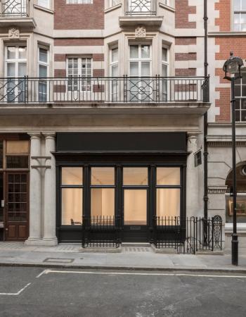 A black shopfront with large, lit display windows showing an empty interior, below a balcony.
