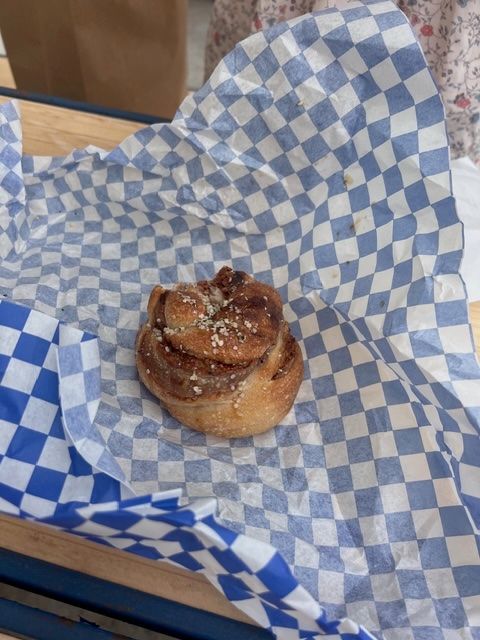 A cinnamon roll topped with white sprinkles sits on blue and white checkered paper.