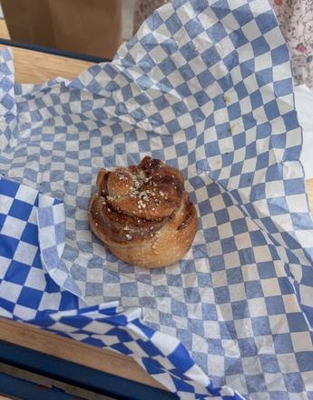 A cinnamon roll topped with white sprinkles sits on blue and white checkered paper.
