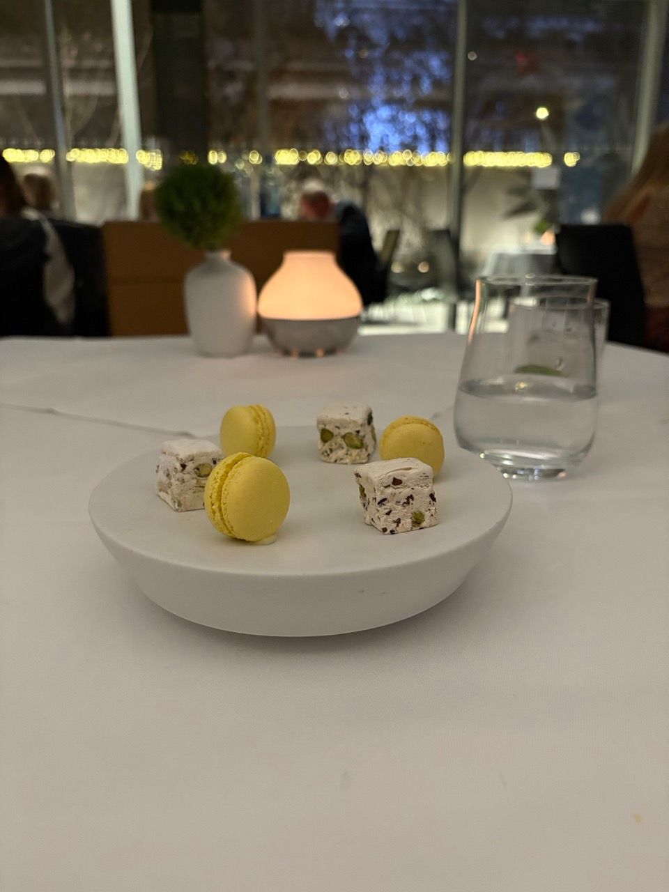 A white plate holds yellow macarons and nougat squares on a table in a restaurant.