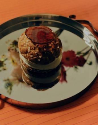 A round pastry with red glaze and sugar crystals sits on a reflective tray showing floral reflections.