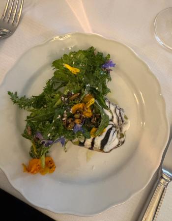Gourmet salad on a white plate, with greens, edible flowers, seeds, and two sauces.