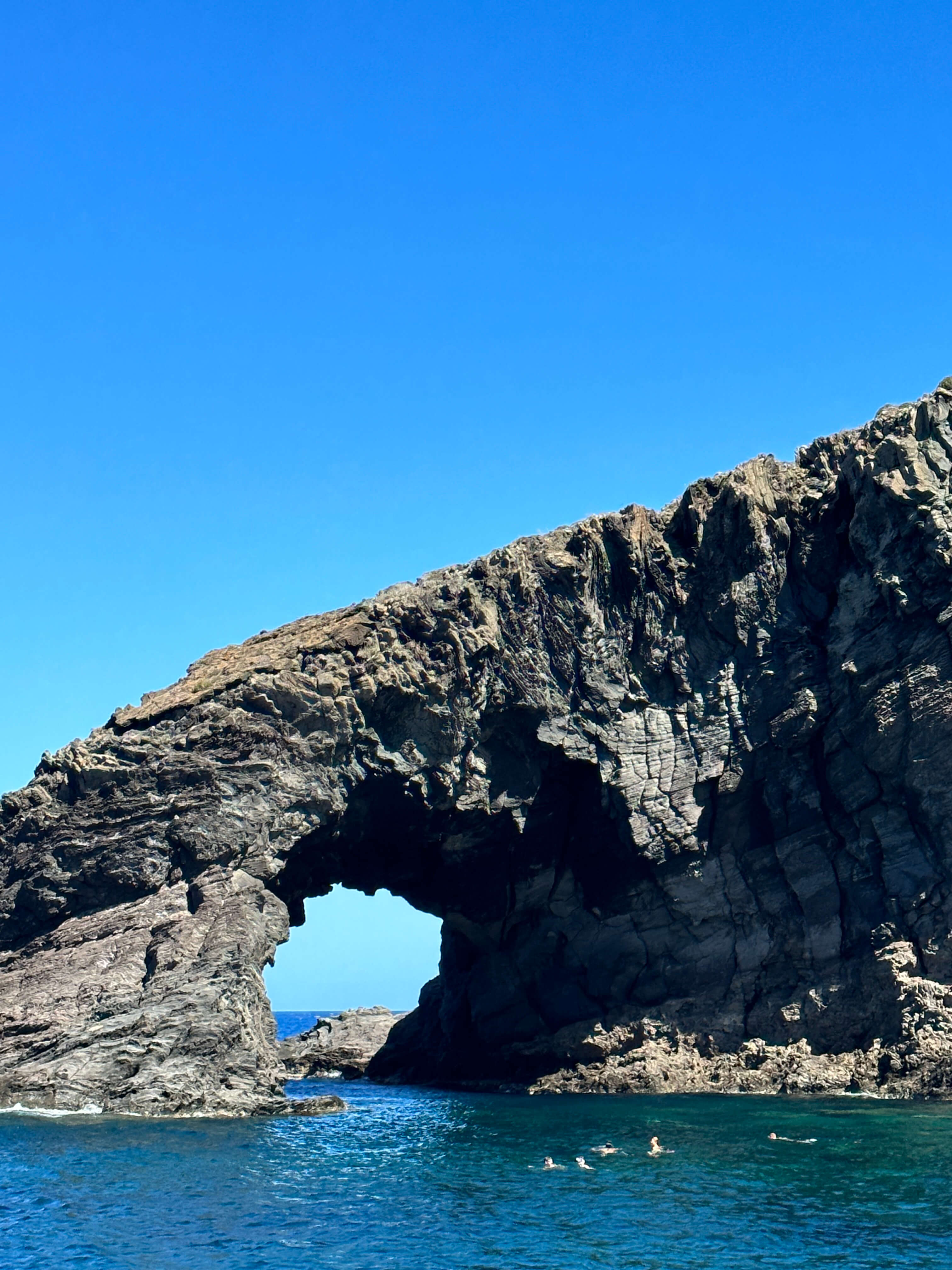 Natural rock arch over blue water with swimmers.