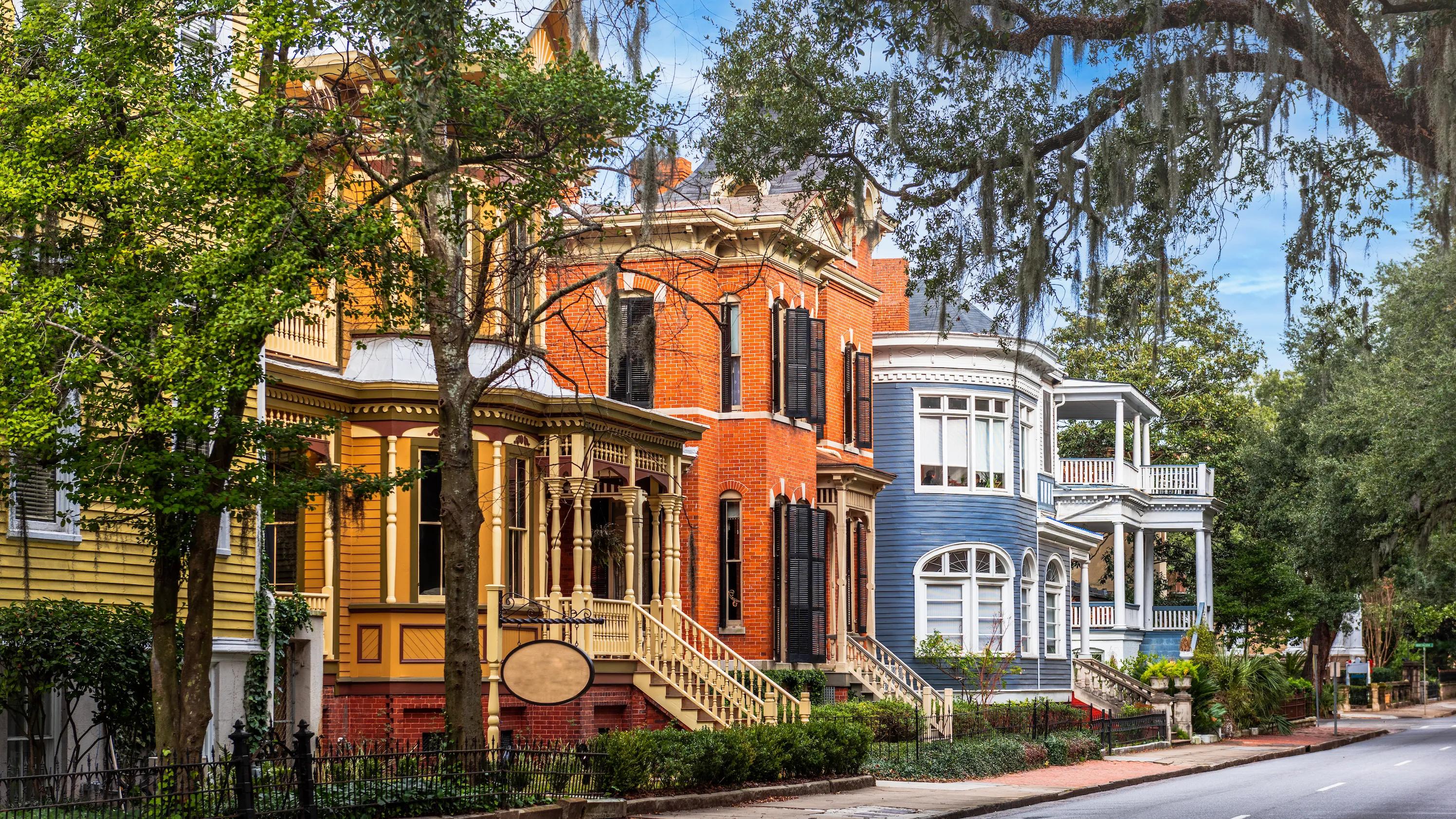 Colorful historic houses with intricate porches and Spanish moss-draped trees lining a street.