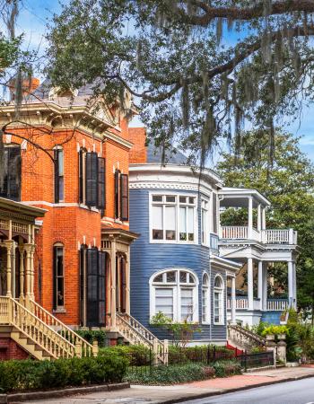 Colorful historic houses with intricate porches and Spanish moss-draped trees lining a street.