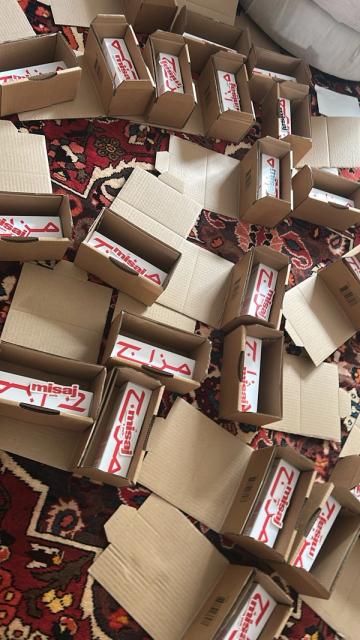 Small cardboard boxes containing white products with red "misaj" branding are scattered on a patterned rug.