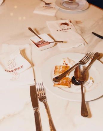 A messy table after a meal with leftover food, used cutlery, and stained napkins on a marble surface.