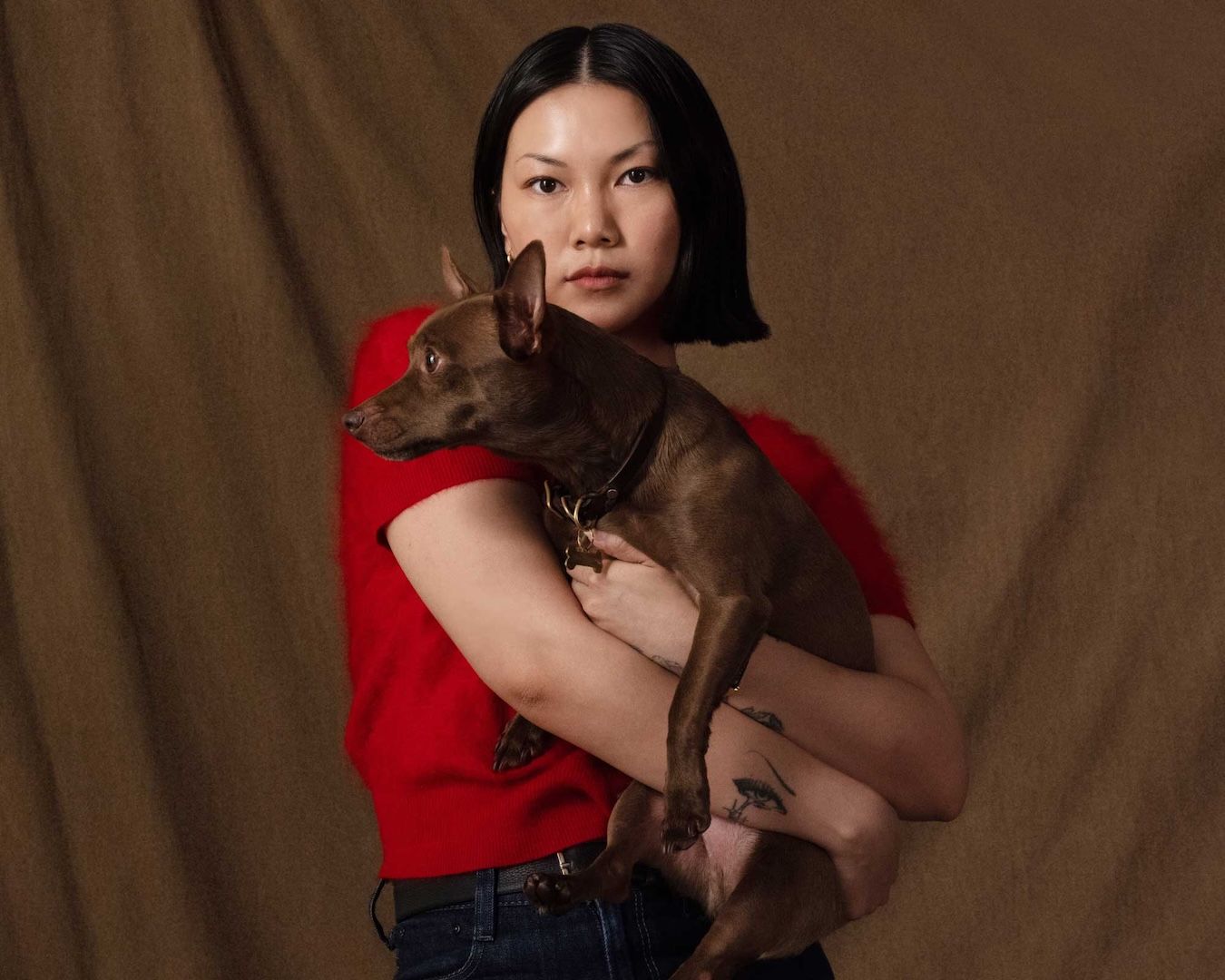Alexandra Pauly holding her dog cam, founder of Biche dog care brand, red top brown background