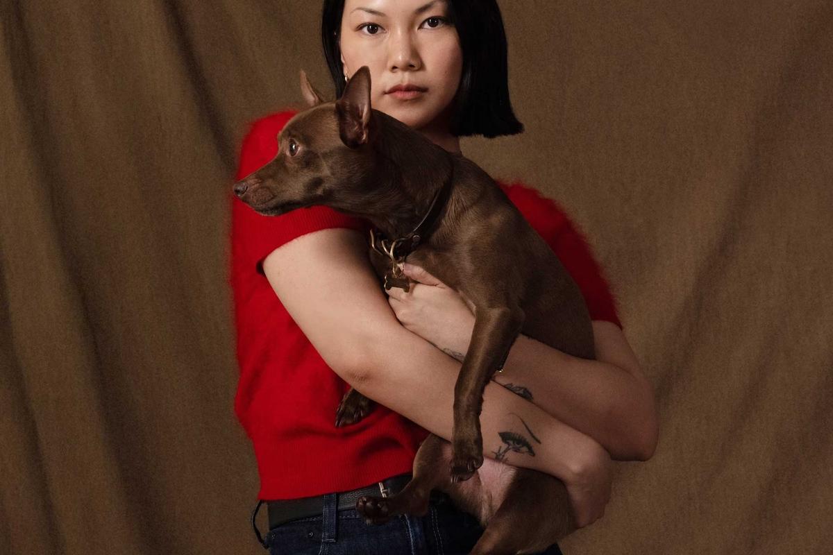 Alexandra Pauly holding her dog cam, founder of Biche dog care brand, red top brown background