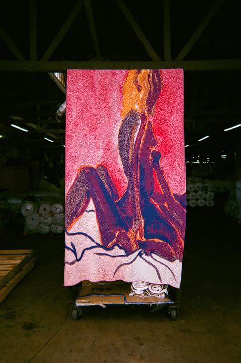An artist's hands mix paint with a palette knife on a paint-splattered wooden table, surrounded by tubes of paint and brushes.