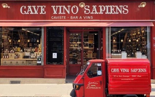 A red wine shop named Cave Vino Sapiens with a matching red three-wheeled delivery vehicle parked in front.