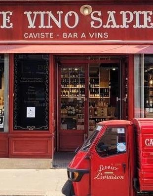 A red wine shop named Cave Vino Sapiens with a matching red three-wheeled delivery vehicle parked in front.