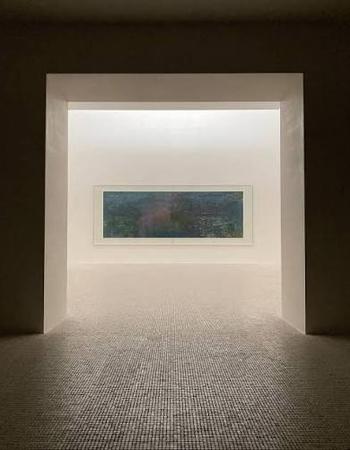Dark doorway opening into a bright room with a long horizontal painting on a white wall and a textured floor.
