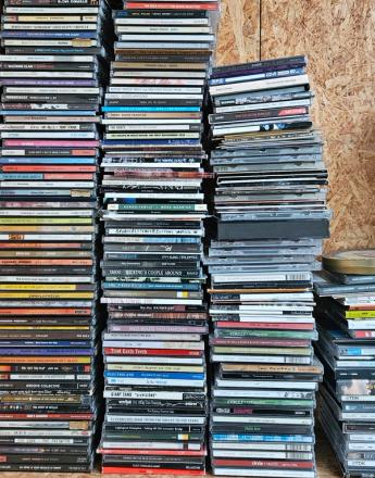 Tall stacks of CDs on a wooden shelf against an OSB wall.