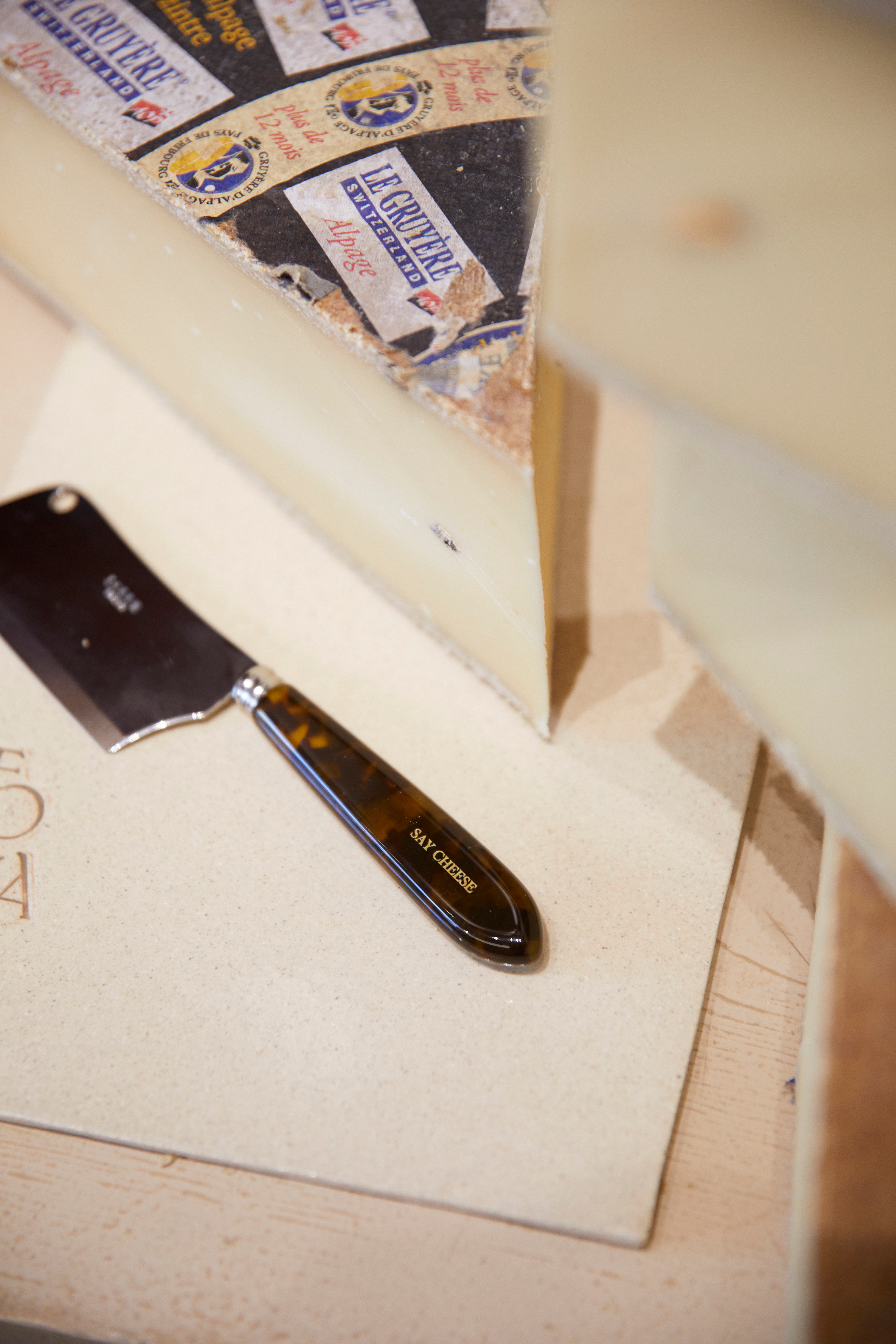 A wedge of Gruyere cheese with its labeled rind and a "Say Cheese" cleaver.