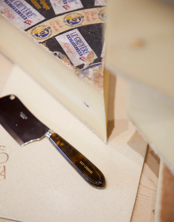 A wedge of Gruyere cheese with its labeled rind and a "Say Cheese" cleaver.