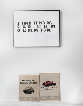 A framed poster with stylized black text hangs above two vintage Volkswagen car advertisements on a white shelf.