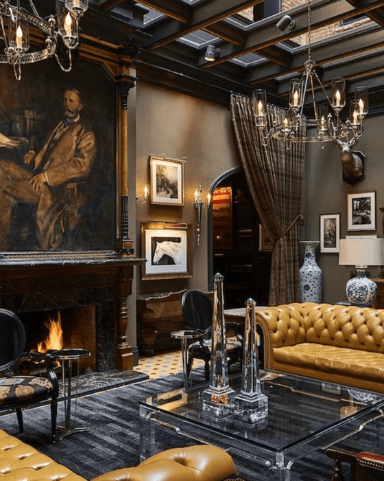 Luxurious living room with fireplace, portrait, tan leather sofas, glass table, and chandeliers.